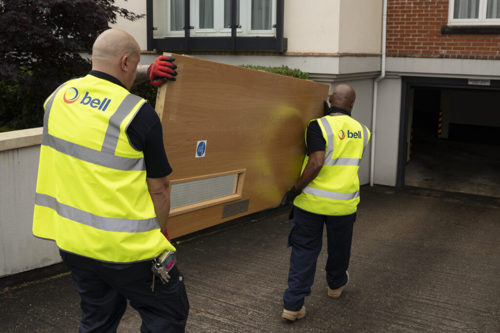 2 Bell Group staff members in high visibility jackets delivering a fire safety door as part of a passive fire fitting in a commercial property.